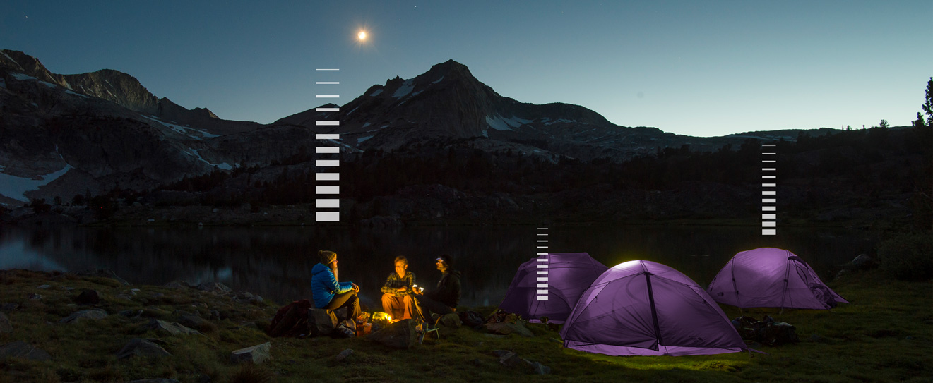 3 backpackers around a campfire with purple tents on a mountaintop