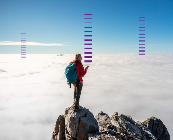 A male hiker with a blue backpack, red jacket and cell phone at the top of a mountain admiring the expanse of clouds in front of him
